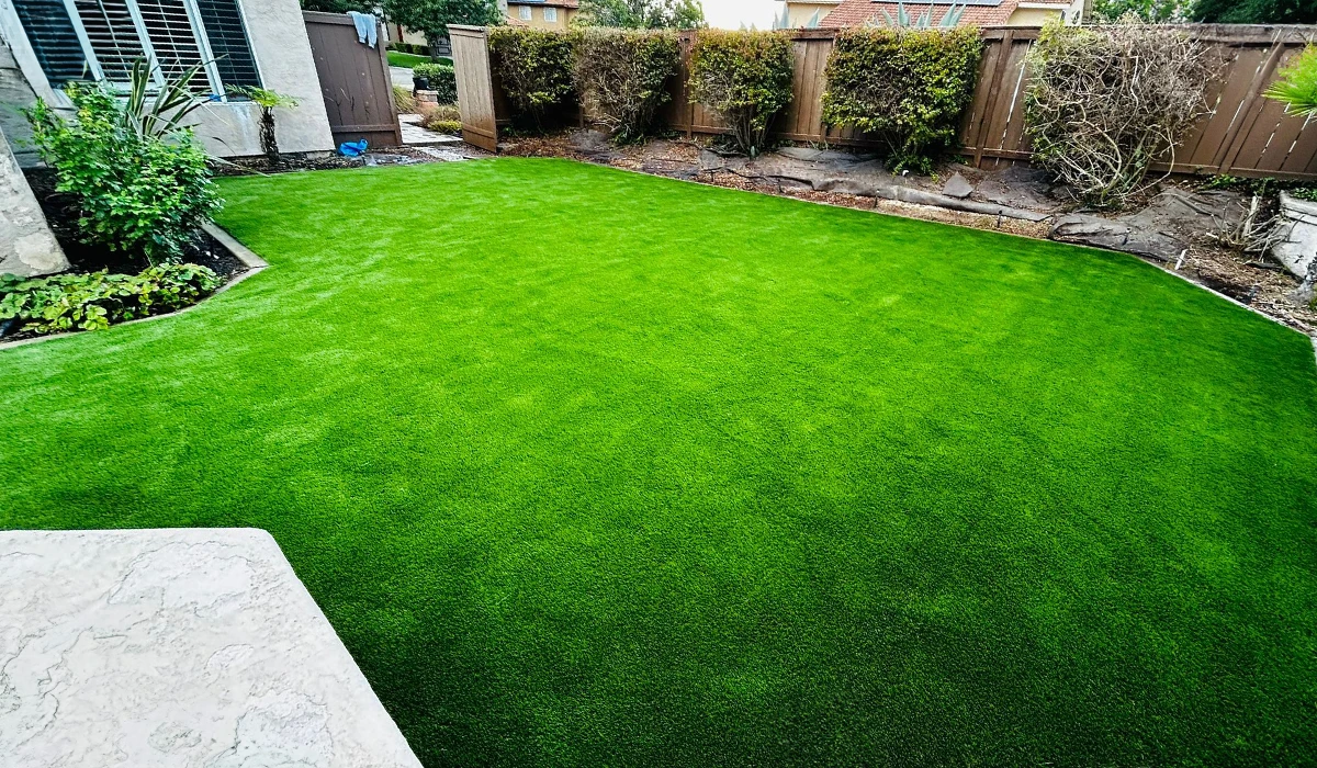 Green artificial grass lawn with surrounding landscaping and wooden fence