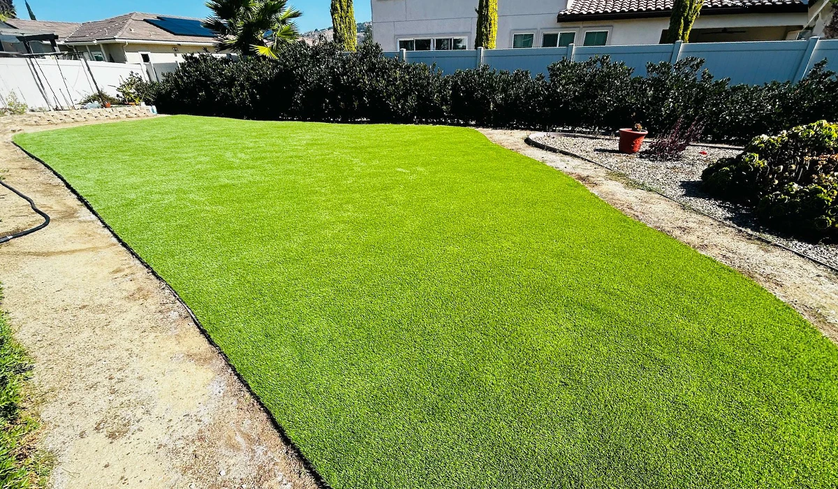 Green artificial grass covers a flat area in a landscaped yard