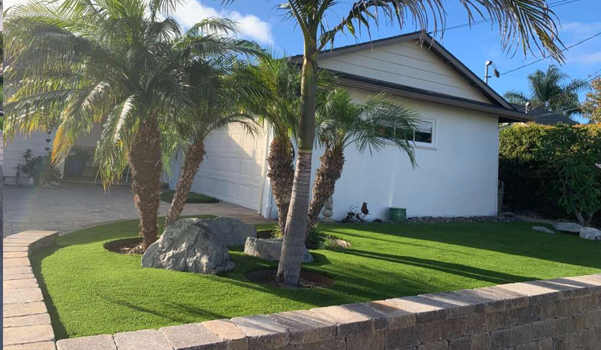 A house with palm trees and a green lawn, surrounded by a stone border