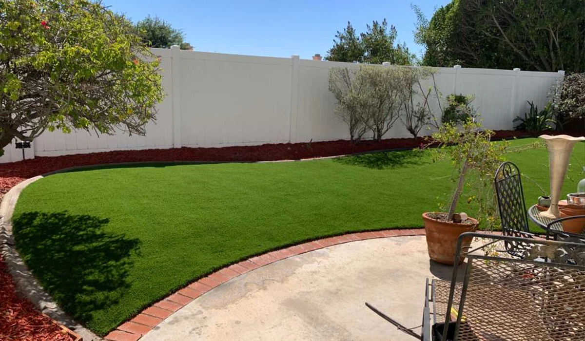 Lawn area with green grass, surrounded by a white fence and landscaped shrubs