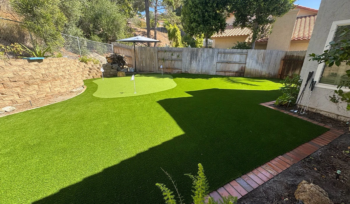 A backyard with a green synthetic lawn and a small putting green area