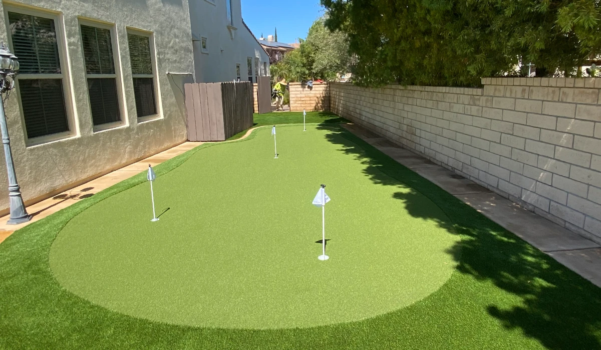 Artificial grass putting green with two holes, surrounded by walls and a pathway