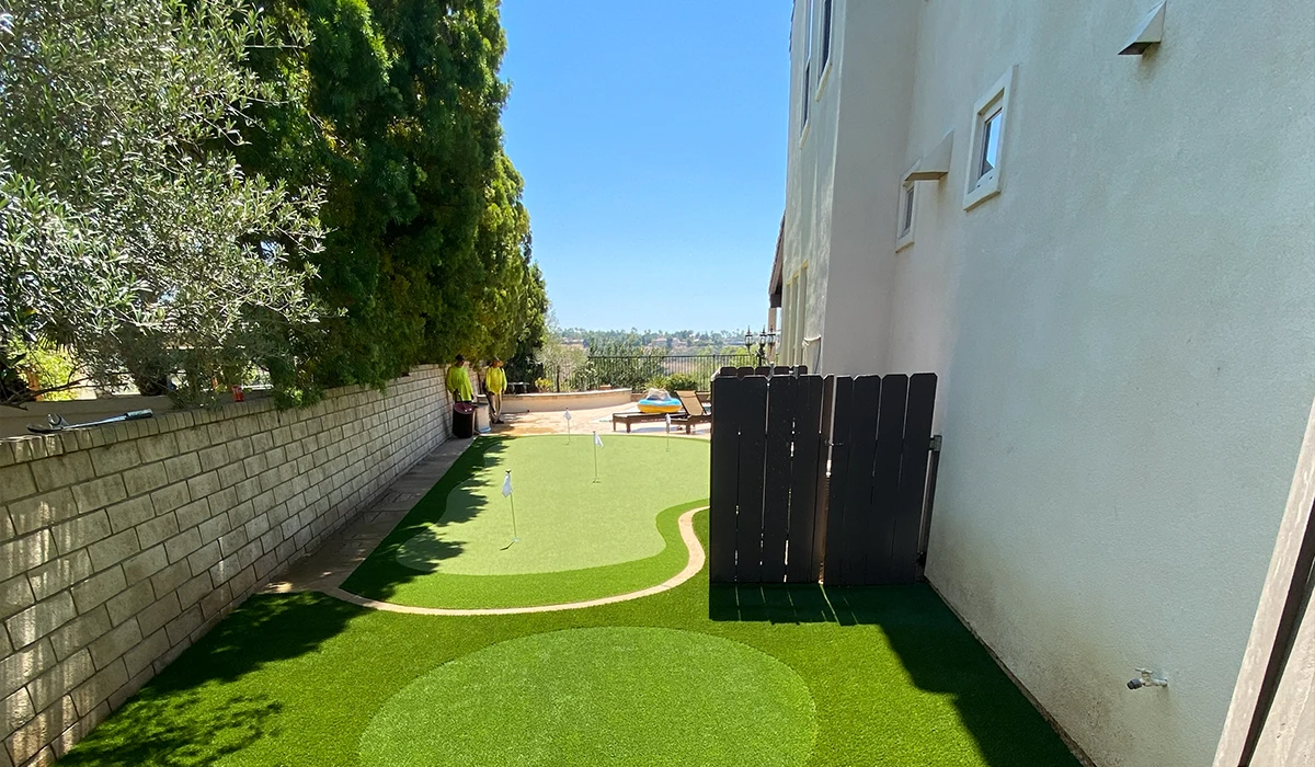View of a landscaped yard with artificial grass and a wooden fence. Clear blue sky above