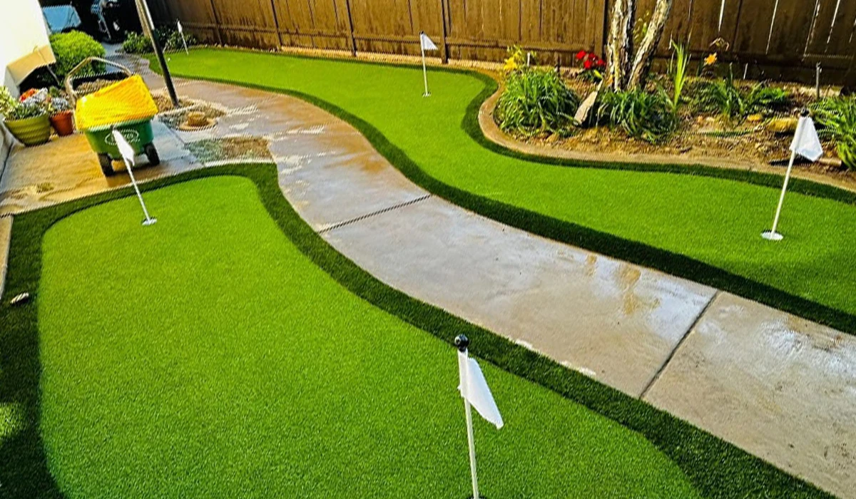Lawn with a winding path and small flags, surrounded by greenery and a wooden fence