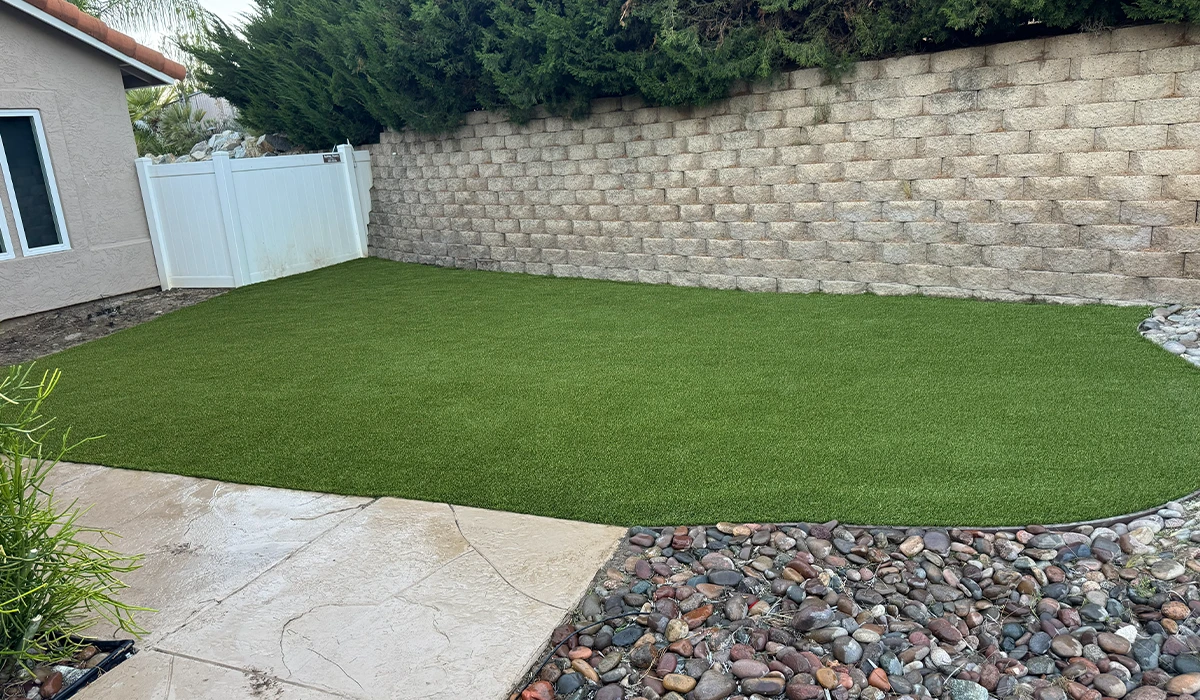 Artificial grass lawn in a yard next to a stone pathway and a block wall