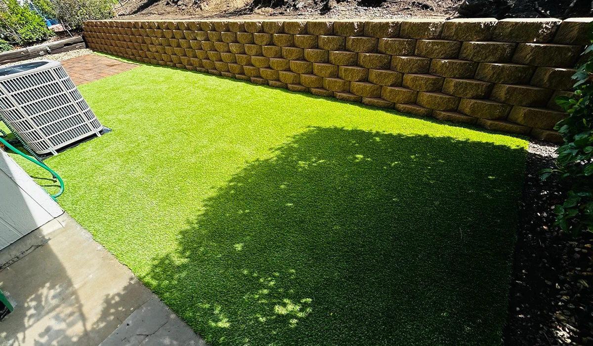 Artificial grass area next to a stone wall and an air conditioning unit