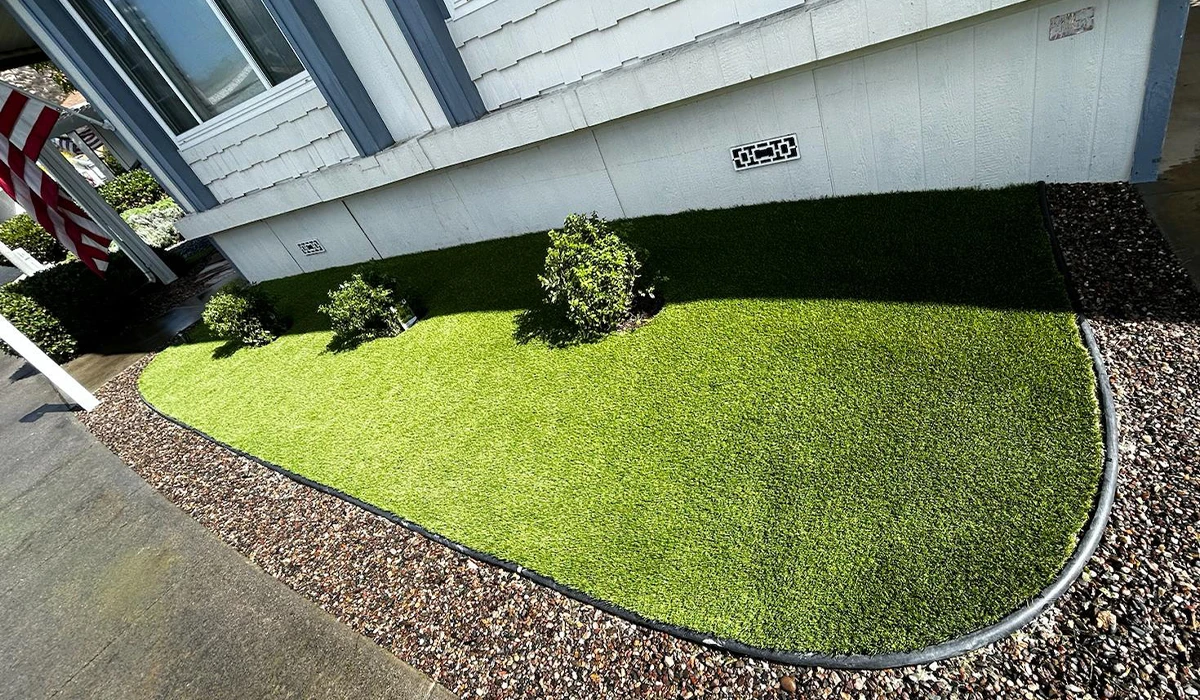 A landscaped area with artificial grass and small bushes, bordered by gravel