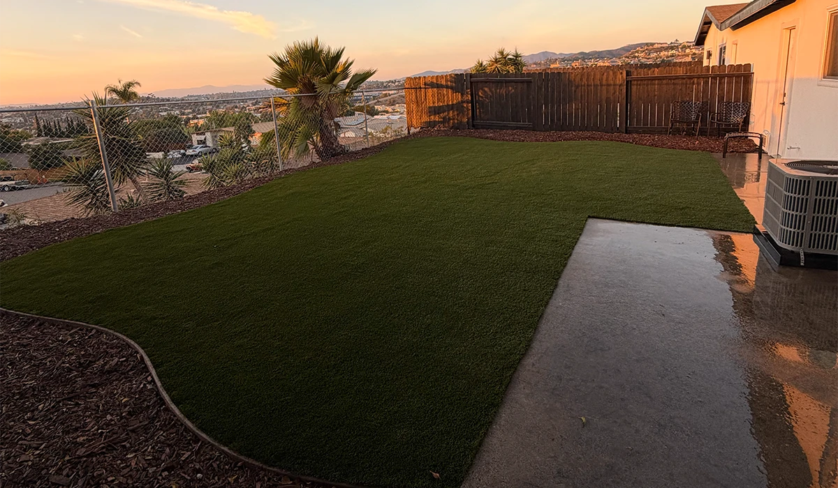 Backyard with artificial grass, a patio, and a wooden fence at sunset