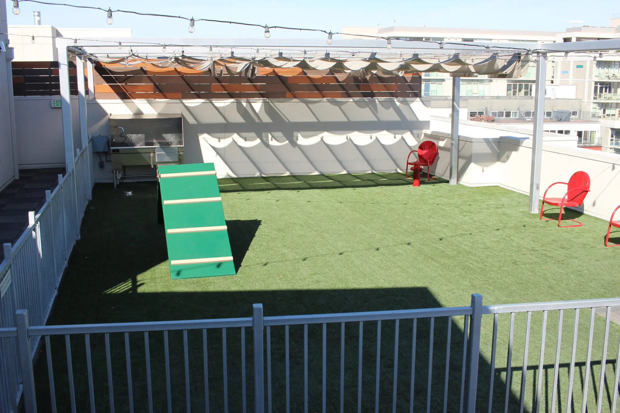 Rooftop space with artificial grass, seating, and sloped green ramp under a shaded area