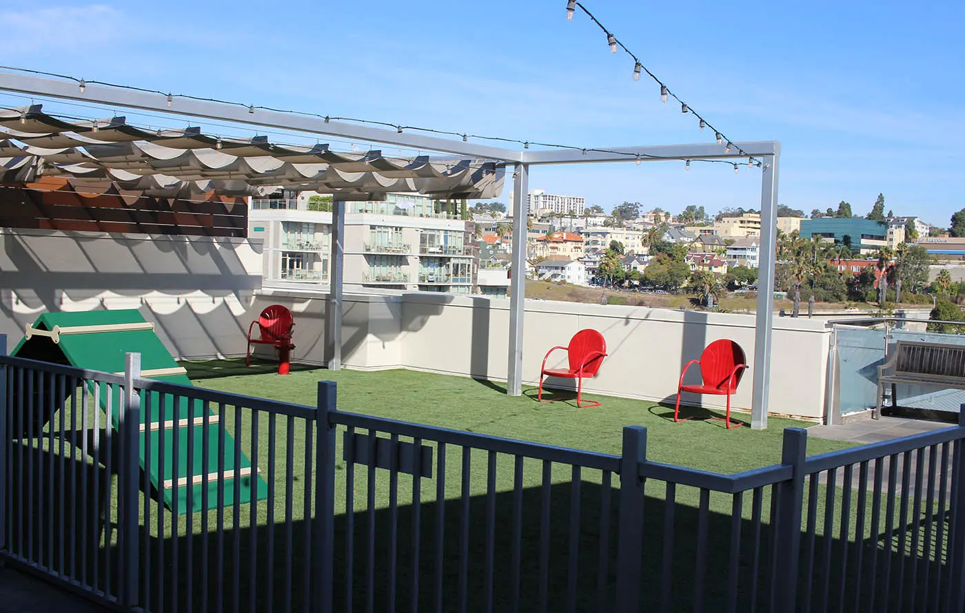 Rooftop patio with green grass, red chairs, and a shaded seating area. City view in background