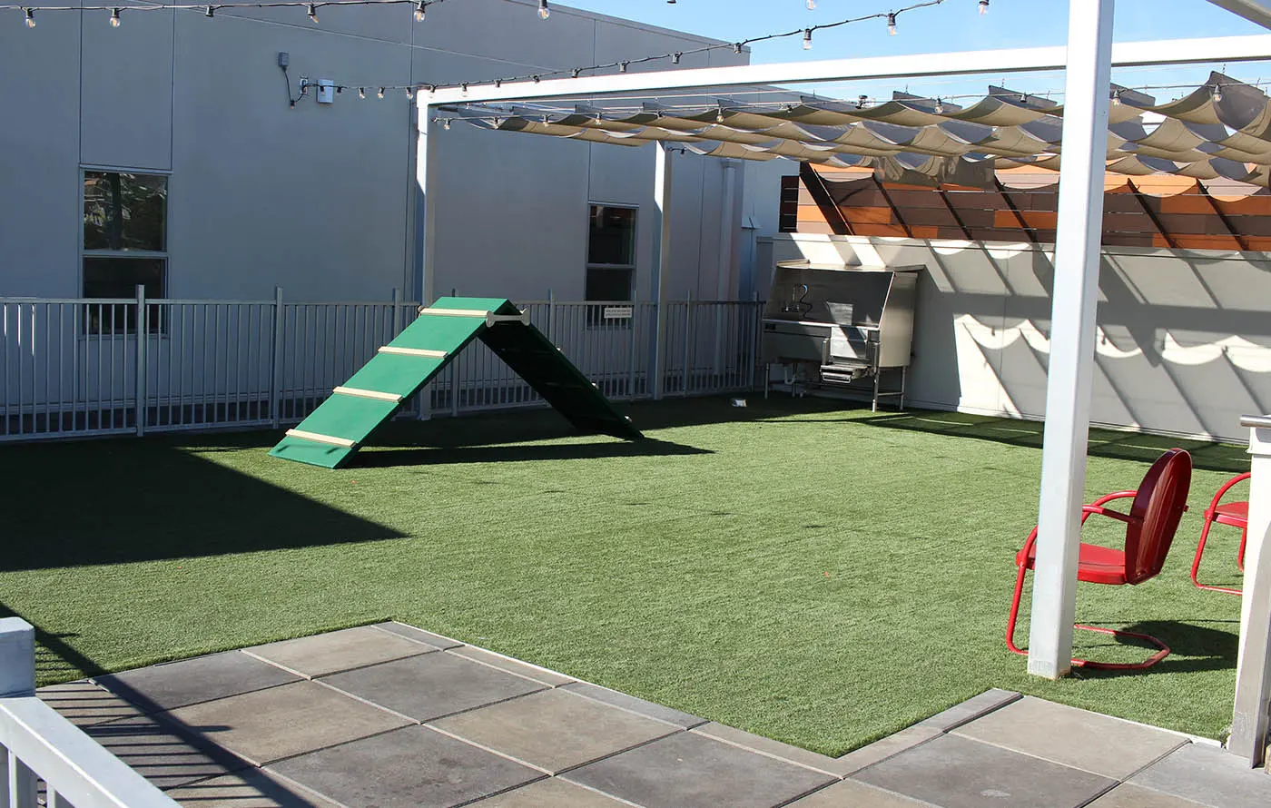 A rooftop area with artificial grass, a climbing ramp, and red chairs under a pergola