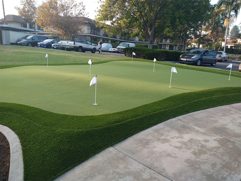 A putting green with multiple flags and a parking lot in the background