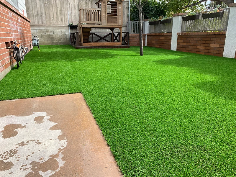 Lush green artificial grass lawn with a wooden play structure in the background