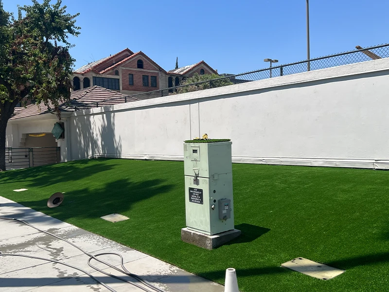 Green artificial lawn with a utility box and a white wall in the background