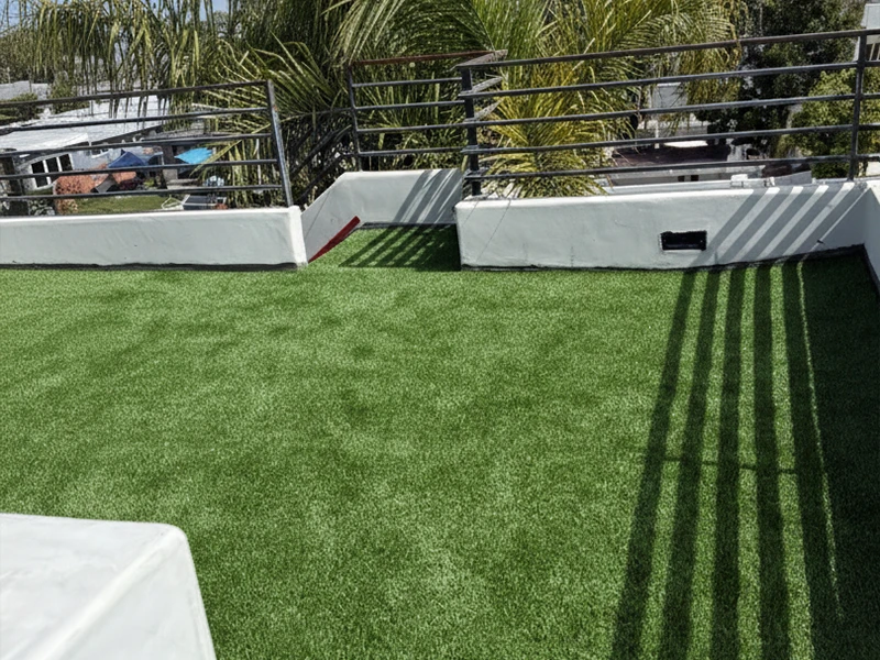 Rooftop space covered in artificial grass with white walls and shadows from railing