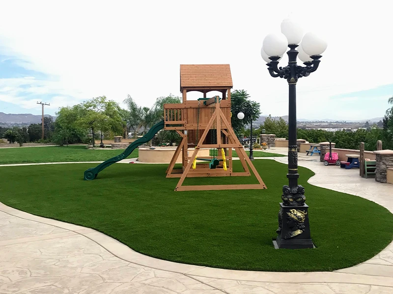 Playground structure with slide and sandbox on lawn, next to a street lamp