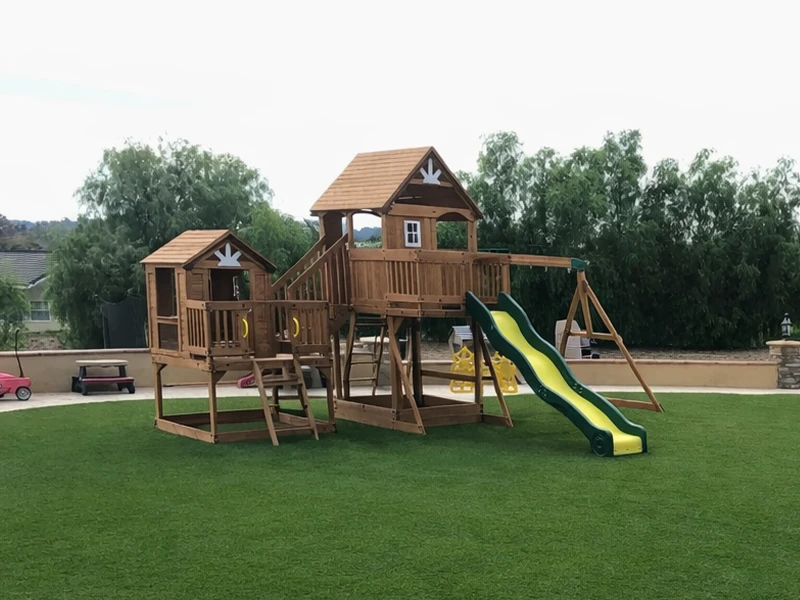 Wooden playground structure with slides and a playhouse, set on grassy area