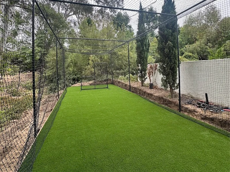 Cricket practice net area with artificial grass and trees in the background