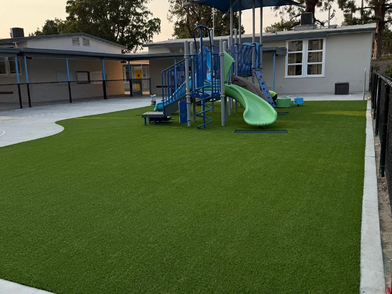 Playground area with green artificial grass and a blue slide and play structure